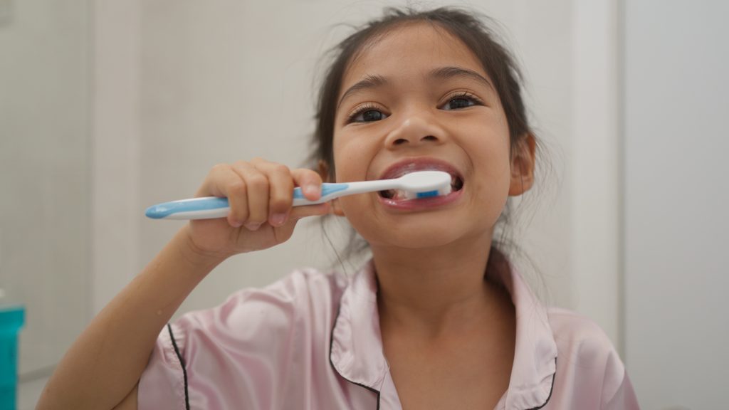 Girl of asian descent brushing teeth in pjs