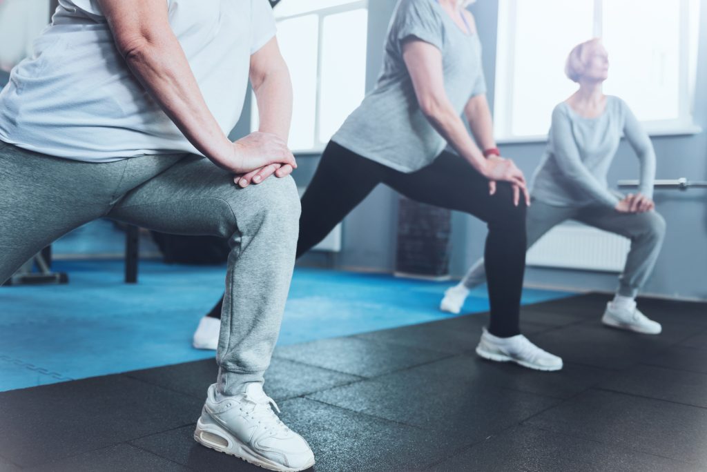 shot of a group of senior ladies standing in a row and doing lunging exercises while all three training in a gym.