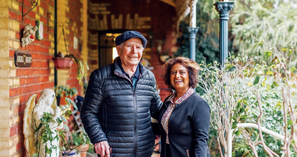 Older man and younger woman standing outside home under veranda