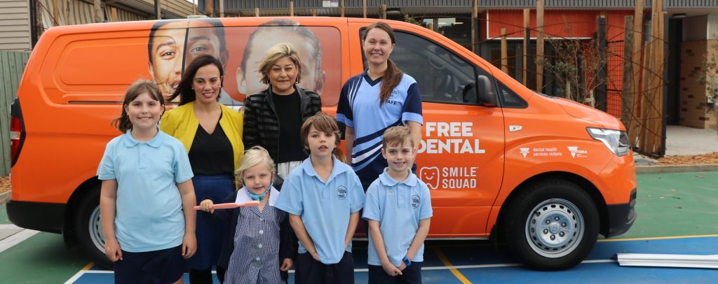 Four primary school children in front of an orange smile squad van with two adult women behind