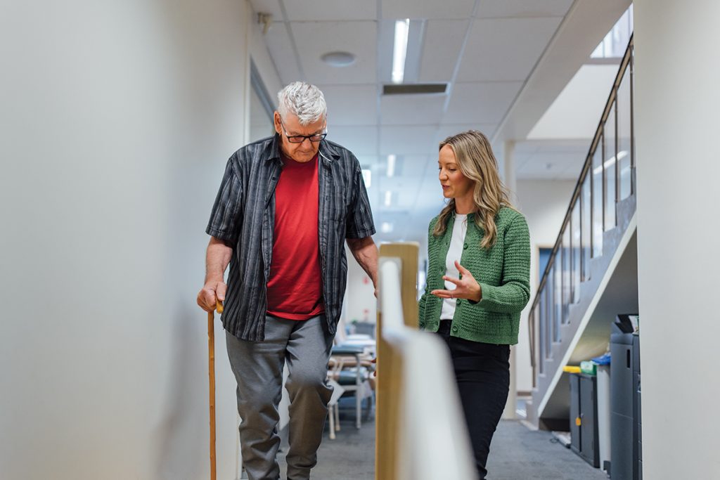 Older man with a cane being assisted by female Occupational Therapist with a hand rail