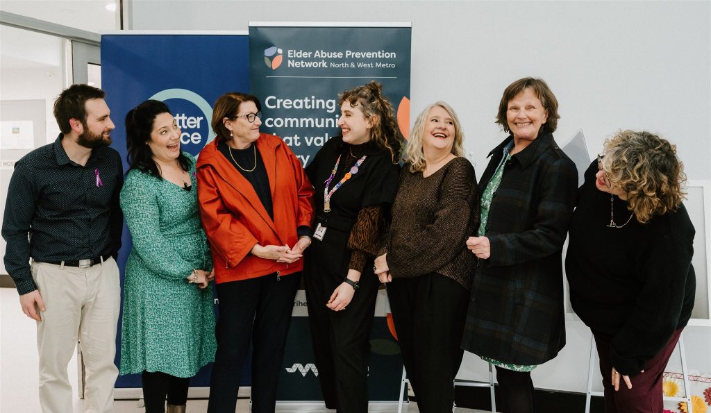 Seven adults smiling in front of Elder Abuse Prevention Network banner