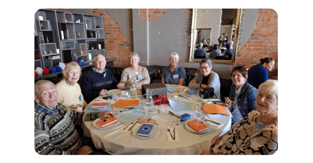 8 people sitting around round table smiling at camera
